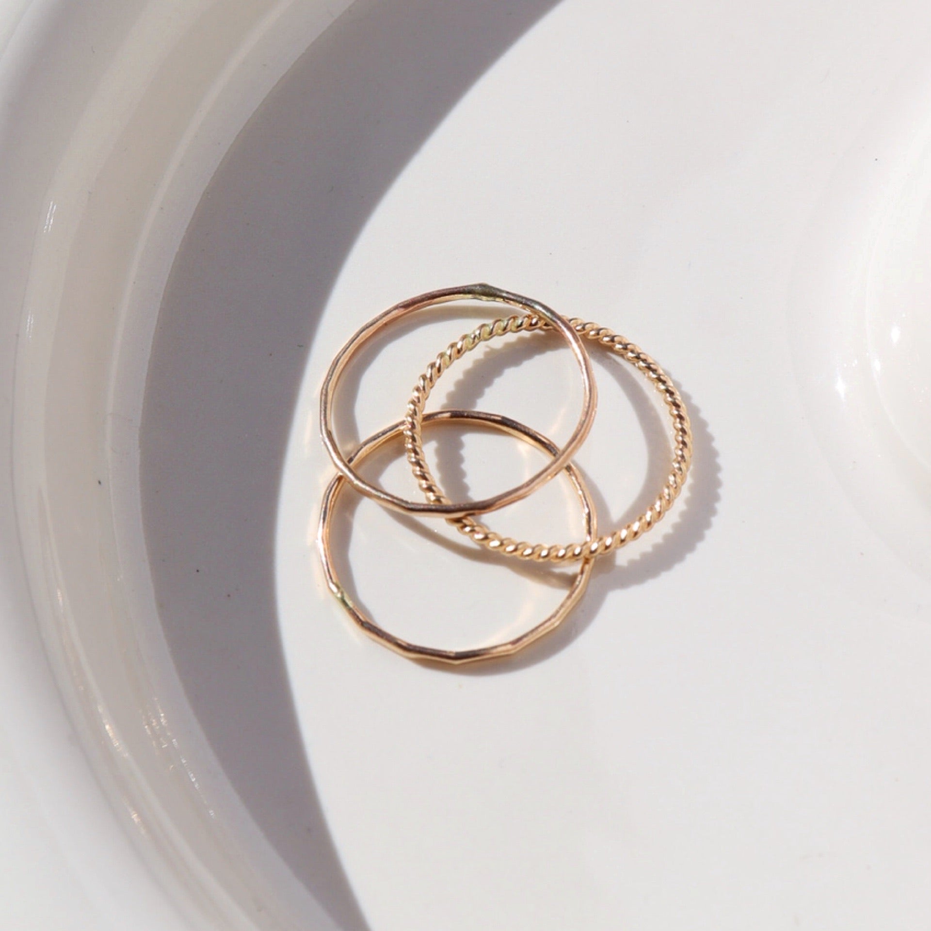 14k gold fill SoHo Ring Set placed on a white plate. This Ring set highlights each one of our go to stacking rings including the stacking ring, spiral ring, and sequins ring. These rings are made to live in made to wear everyday.