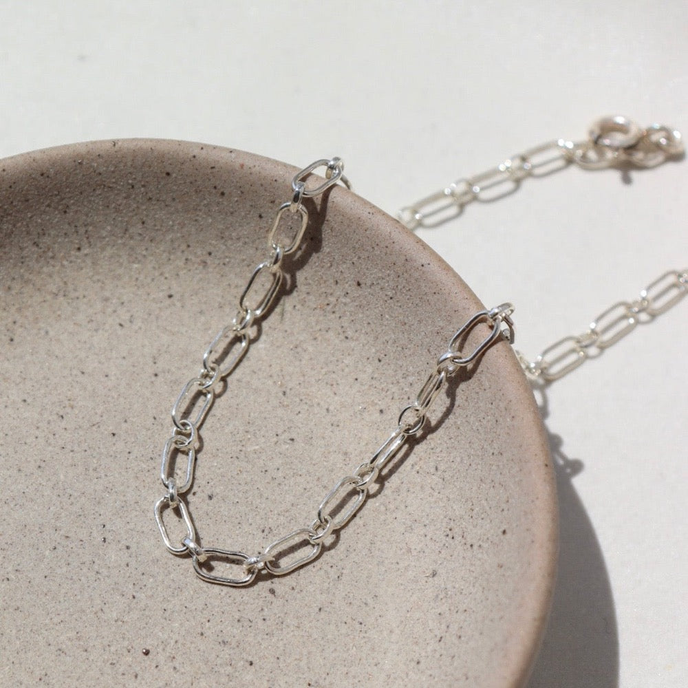 925 Sterling silver Brooklyn Anklet laid on a tan plate in the sunlight.