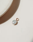 Large freshwater pearl on a round gold fill connector laid on a beige background in the sunlight