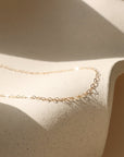 Gold filled dainty heart linked chain necklace on a textured beige surface