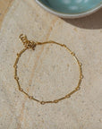 Gold bar link chain, displayed on a stone backdrop.