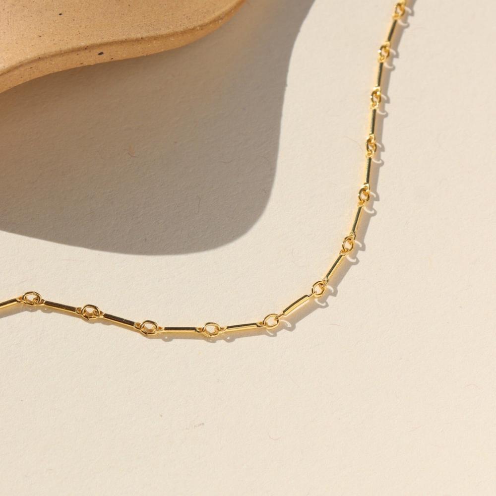 Gold bar link chain, displayed on a cream backdrop.