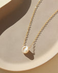 14k gold fill freshwater pearl necklace laid on a peach colored plate. This necklace features the simple chain with the freshwater pearl  wired in the middle.