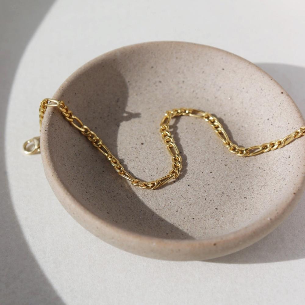 14k gold fill Gigi Bracelet laid on a gray plate set in the sunlight.