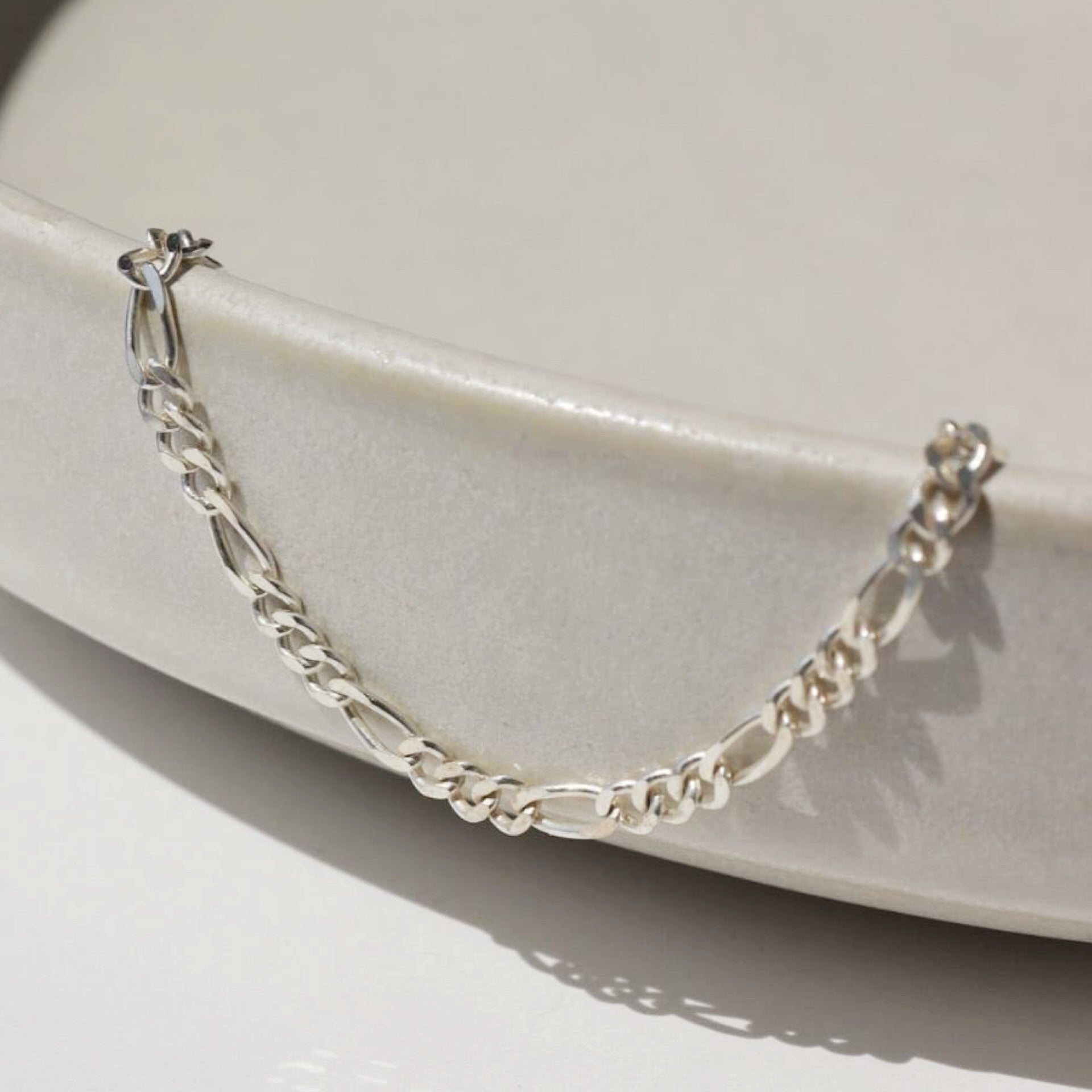 925 Sterling silver Figaro chain anklet placed on a ceramic bowl