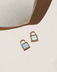 Gold padlock charm with shimmering white and blue opal stones on a neutral surface in warm natural light.
