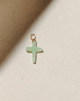 Chrysoprase cross charm featuring a soft green gemstone cross wrapped with gold wire, photographed on a warm neutral surface with soft natural light and shadows.