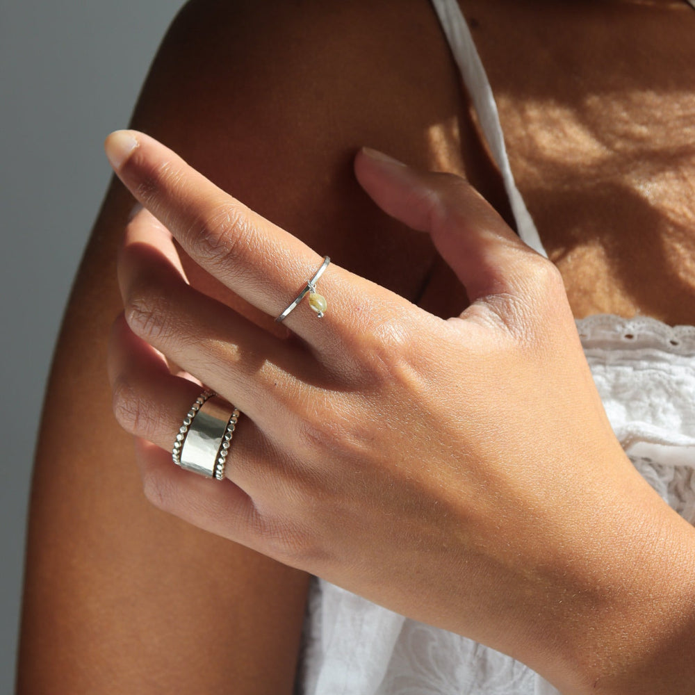 Model wearing a sterling silver ring stack. Featuring a thick sterling silver hammered band stacked between two sequin rings.
