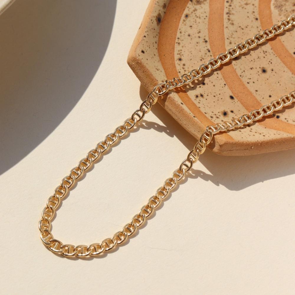 The Marina Chain by Token Jewelry, a modern classic with interlocking oval-shaped links, photographed laying over a patterned ceramic dish
