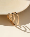 A thick hammered hoop offered in three sizes (small, medium, and large) displayed hanging on a tan dish.