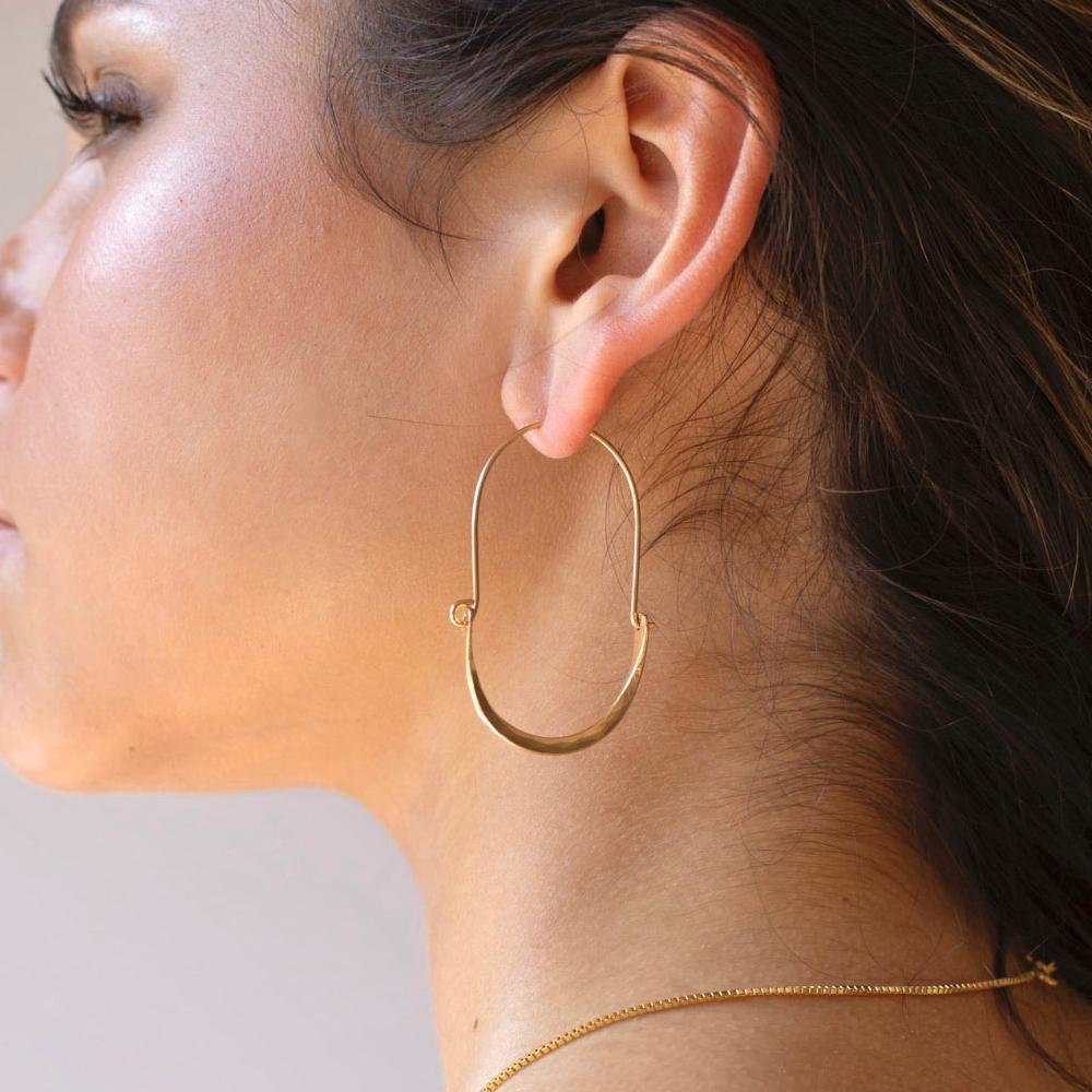 Hammered Paloma earrings taken a brunette model. These earrings feature a wire around 1/2 inch shaped like an oval, then followed by the other half of the oval that is hammered. Model is also wearing a thin gold chain also known as our Delaney chain.