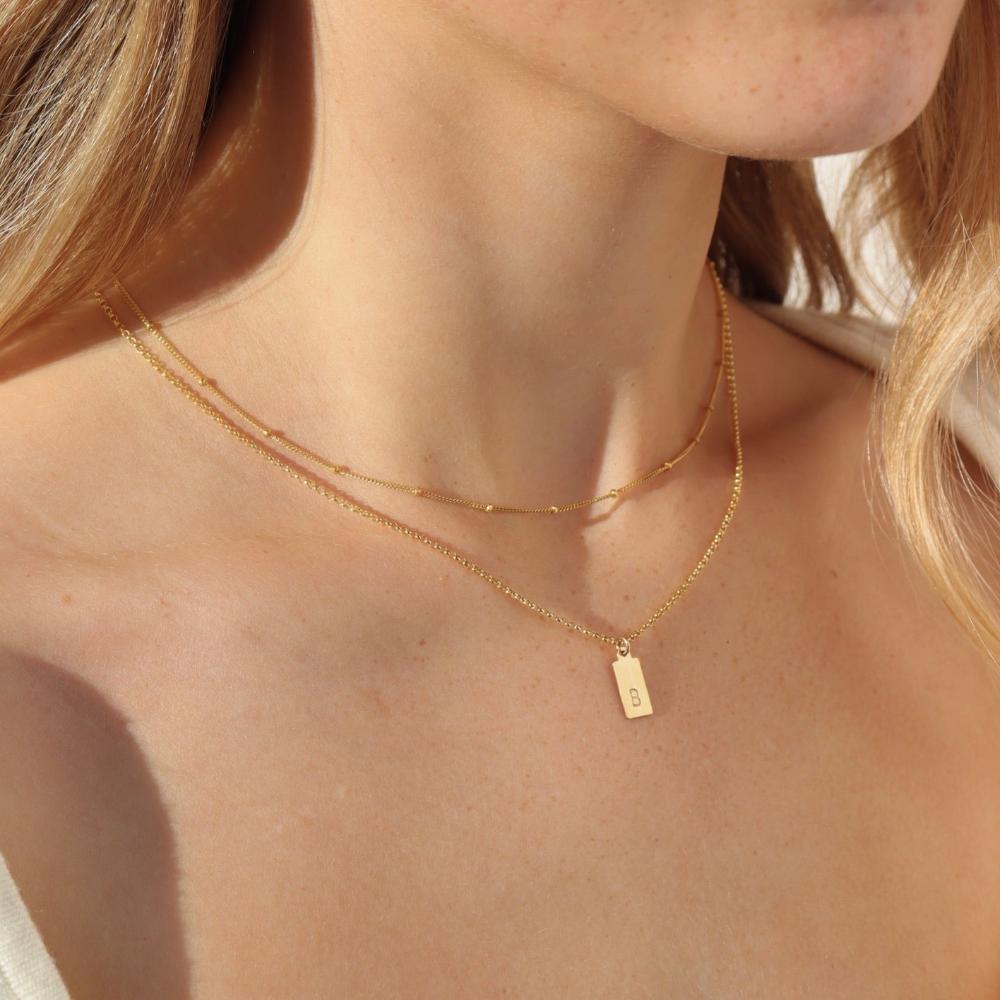Red head model wearing the mini monogram tag necklace. This necklace features a gold rolo chain with a small stamped "B" rectangle pendant.