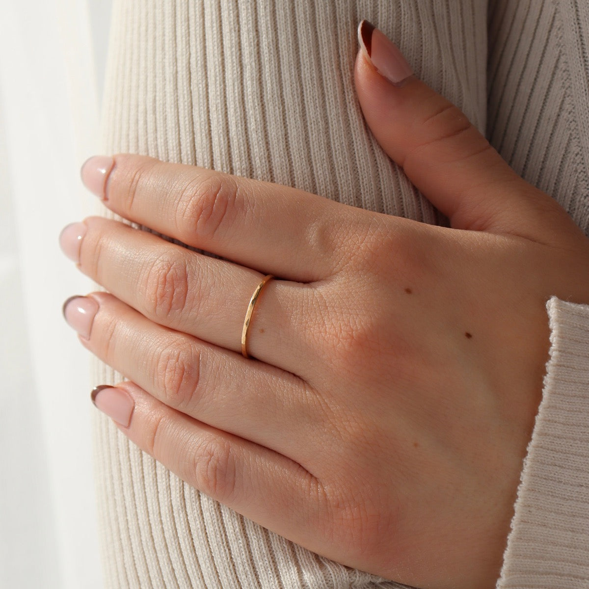 Model is wearing the Essential stacking ring on hear middle finger grabbing her upper arm. These rings are lightly hammered gold stacking ring, handmade by Token Jewelry in Eau Claire, Wisconsin