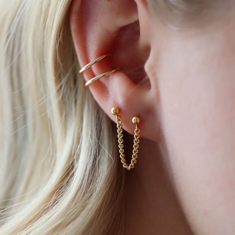 Two gold ball posts connected with a curb chain. Model is also wearing a double ear cuff with a thin wire.