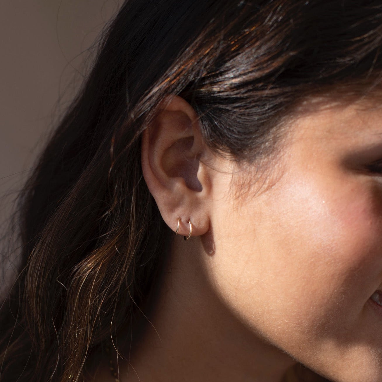 14k gold fill Mini Twist Earrings laid on a peach colored plate in the sunlight. These earring have a little twist giving the allusion that you have two piercings.