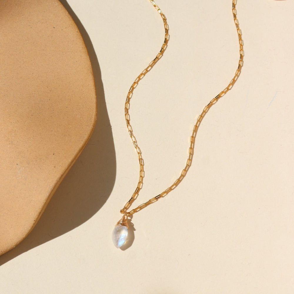 A 14k gold fill box chain featuring a Marquise Moonstone Gemstone wired wrapped at the end. Necklace is displayed on a cream back drop.