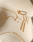 Gold jewelry including a necklace, ring, and earrings on a beige stone surface.