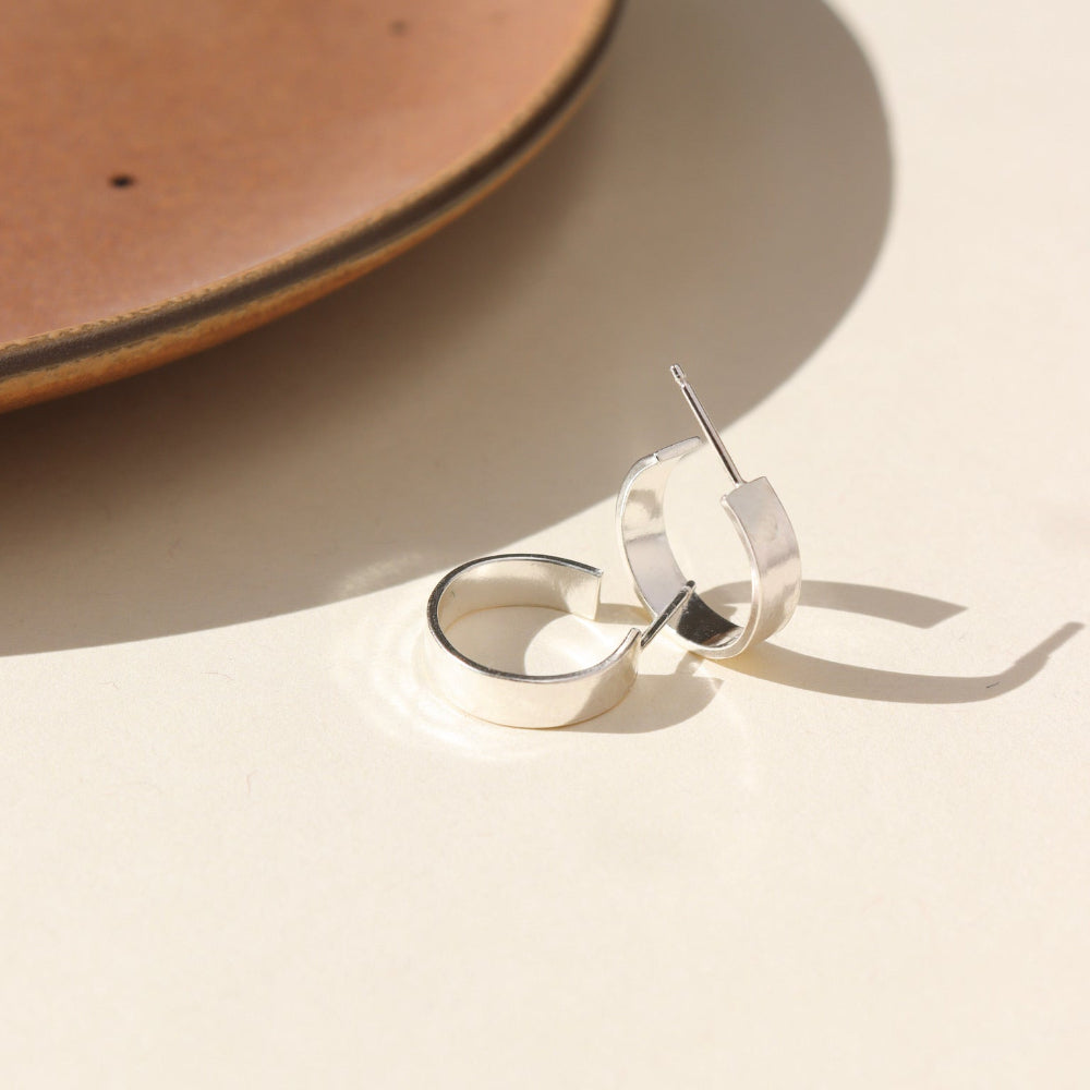 A small thick hammered sterling silver hoop displayed on a cream back drop.