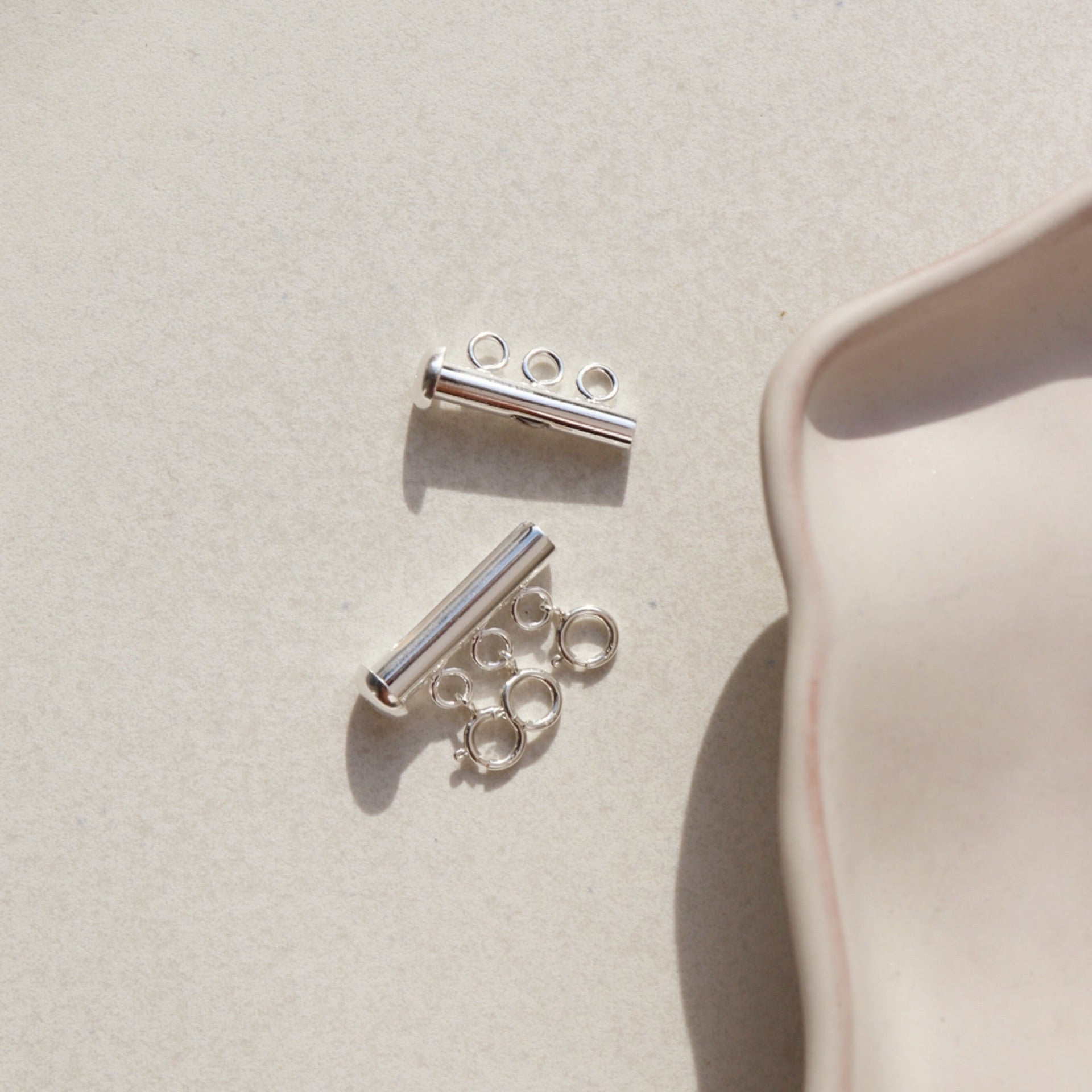 A silver necklace layering clasp with three necklace attachment points laid on a cream backdrop.