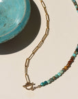 Taos Toggle Necklace featuring half turquoise beads and half gold paperclip chain with a front toggle clasp displayed against a cream back drop