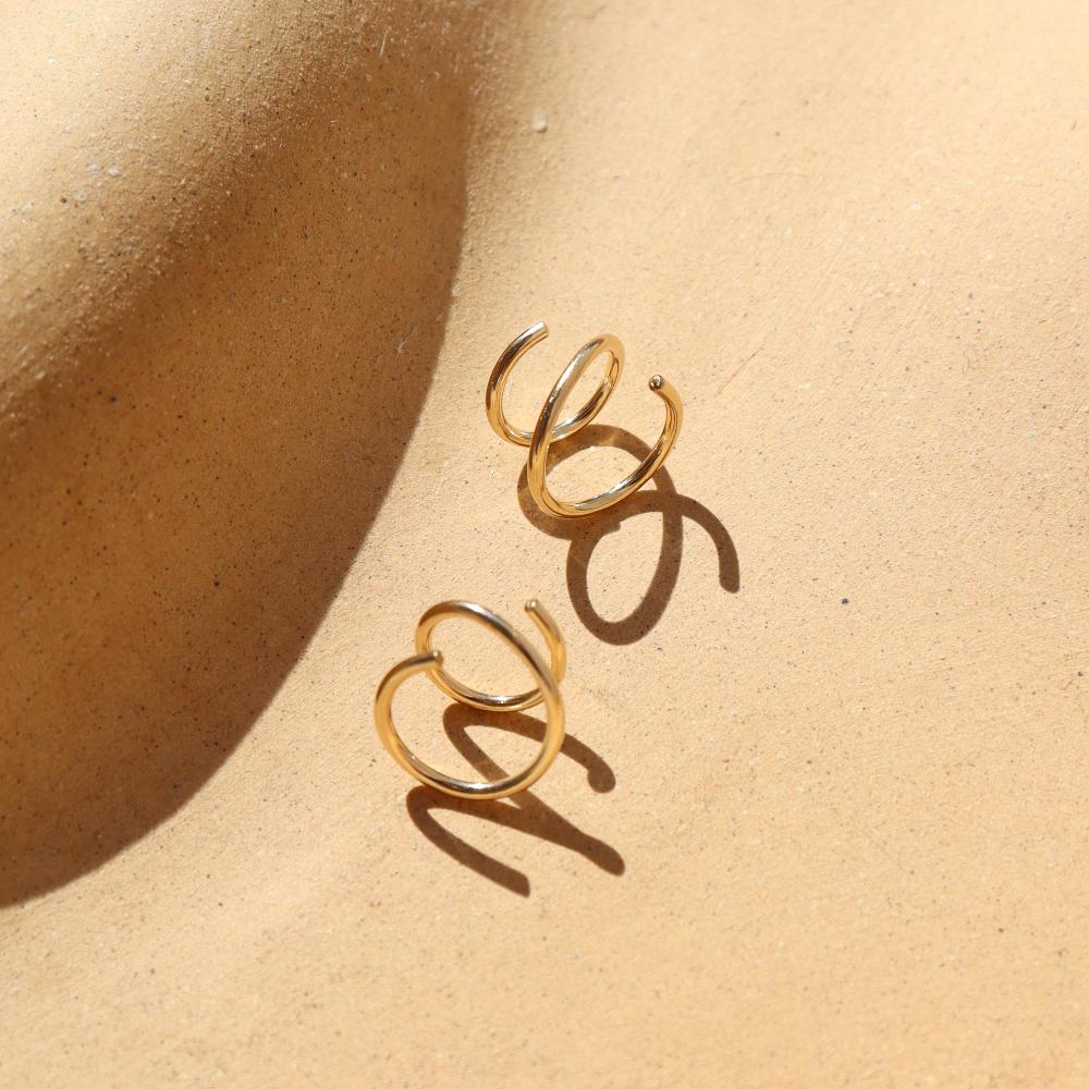 14k gold fill Mini Twist Earrings laid on a peach colored plate in the sunlight. These earring have a little twist giving the allusion that you have two piercings.