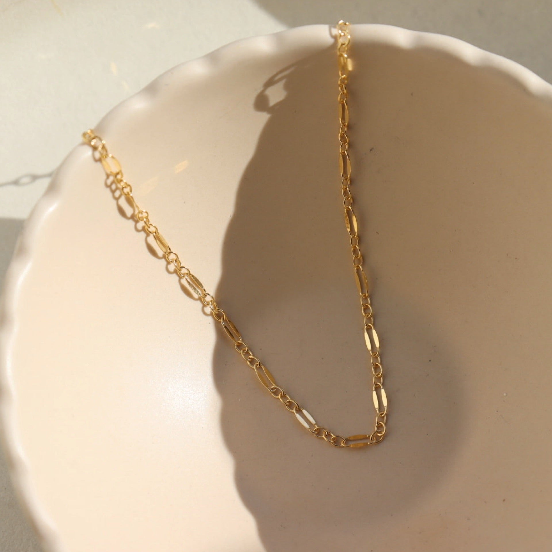 14k gold fill Sylvie choker laid on a tan plate in the sunlight.