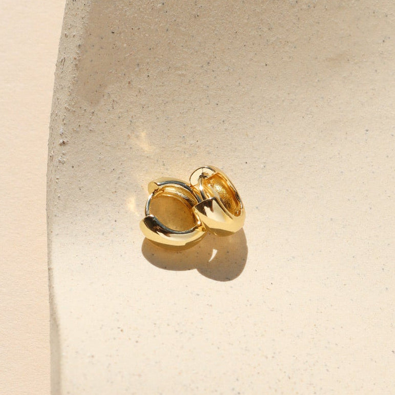 Gold earring on a white cushion against a beige background