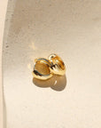 Gold earring on a white cushion against a beige background