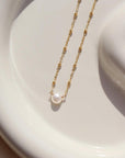 14k gold fill Beaded pearl necklace laid on a white plate in the sunlight