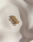 A gold necklace layering clasp with three necklace attachment points laid on a cream backdrop. 