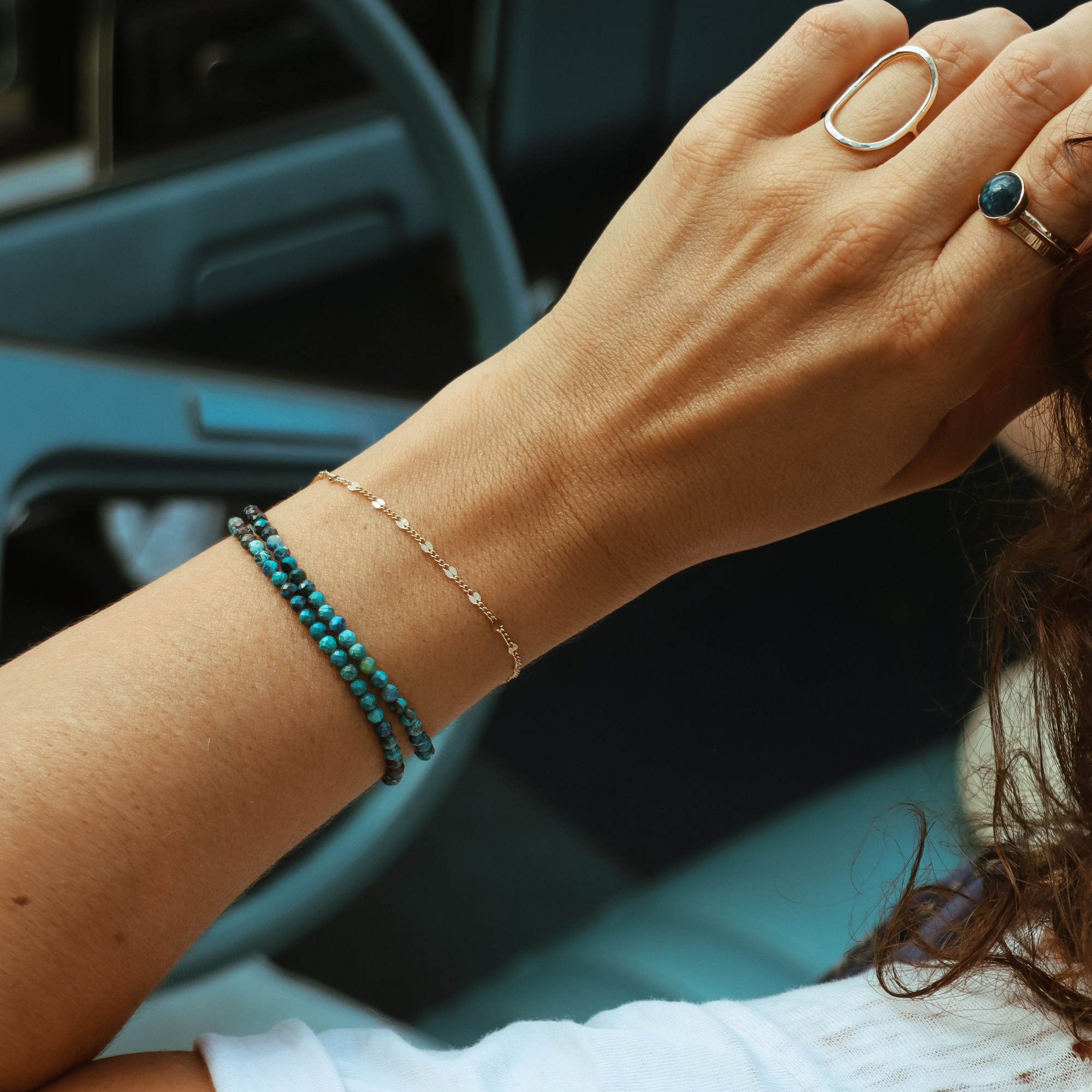Model wearing the 14k Gold Fill Sunburst Bracelet, a delicate gold chain bracelet layered with chrysocolla gemstone bracelets and styled with gold rings in a lifestyle setting.