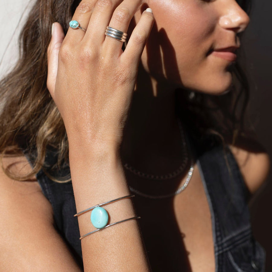 sterling silver double wire cuff bracelet featuring a large turquoise stone wired to the middle. Photographed on a model's arm wearing a black denim skirt, black cowboy boots, and silver rings