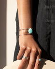 sterling silver double wire cuff bracelet featuring a large turquoise stone wired to the middle. Photographed on a model's arm wearing a black denim skirt, black cowboy boots, and silver rings