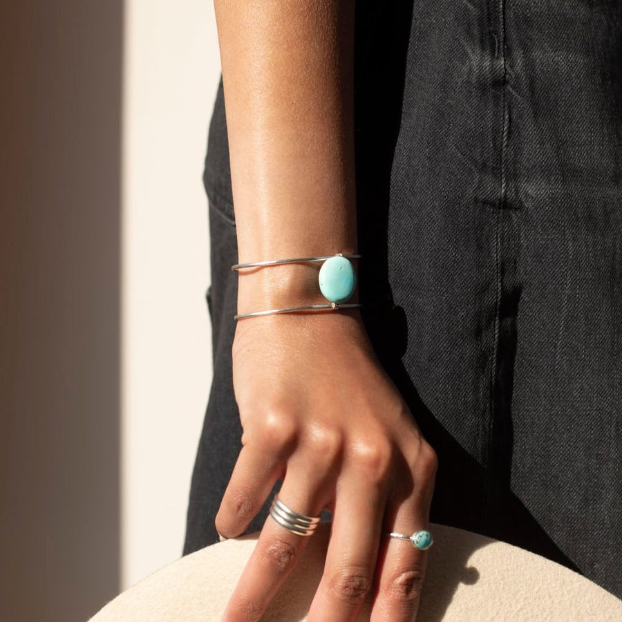 sterling silver double wire cuff bracelet featuring a large turquoise stone wired to the middle. Photographed on a model's arm wearing a black denim skirt, black cowboy boots, and silver rings