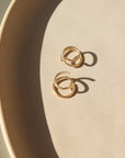 14k gold fill Mini Twist Earrings laid on a peach colored plate in the sunlight. These earring have a little twist giving the allusion that you have two piercings. 