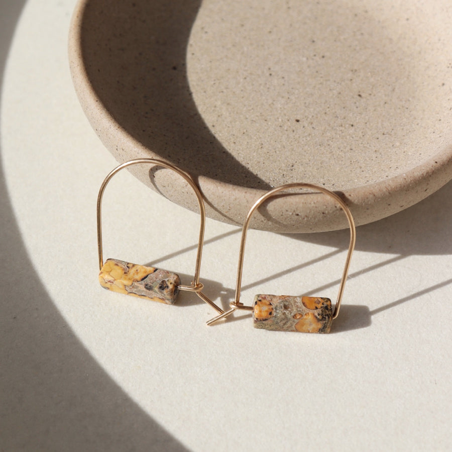 14k gold fill Leopard Skin Jasper Arches placed against a gray plate in the sunlight. 