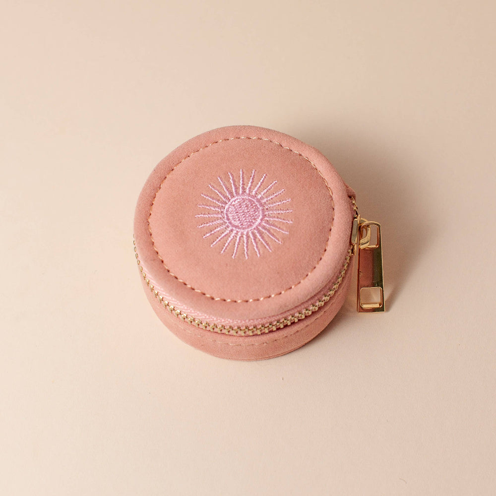 Pink round jewelry case with gold zipper on a beige background