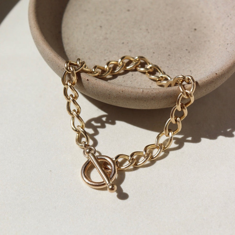 14k gold fill Alexandra Toggle Bracket laid on a tan plate in the sunlight. This bracelet features the Alexandra chai with the toggle link to connect it together.