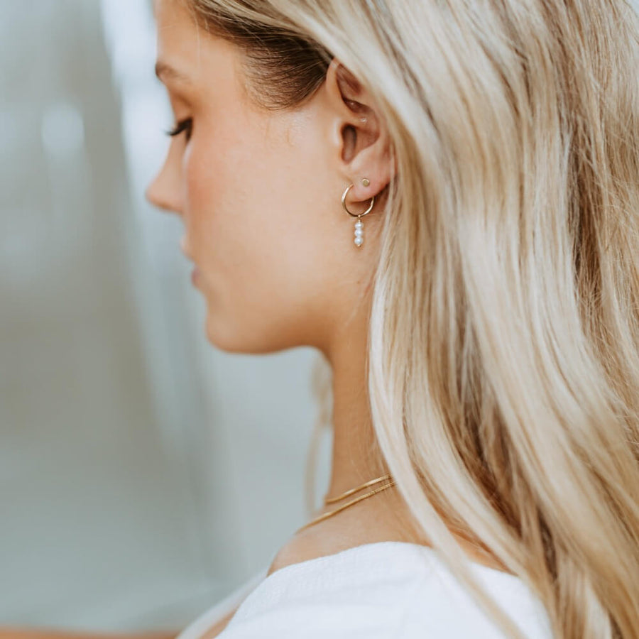 Model wearing 14k gold fill Petite Pearl Hoops, These earrings feature a Goldie hoop with three tiny gemstone studs. - Token Jewelry