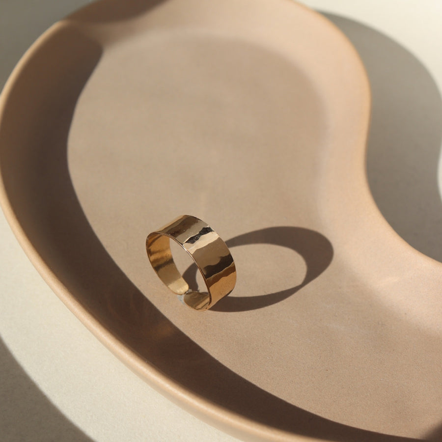 14k gold fill Luxe Ring placed on a tan plate in the sunlight. This ring features Lightly hammered and sophisticated ring cuff.