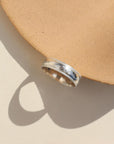 A silver hammered band with rippled edges. Displayed on a small ring dish. 