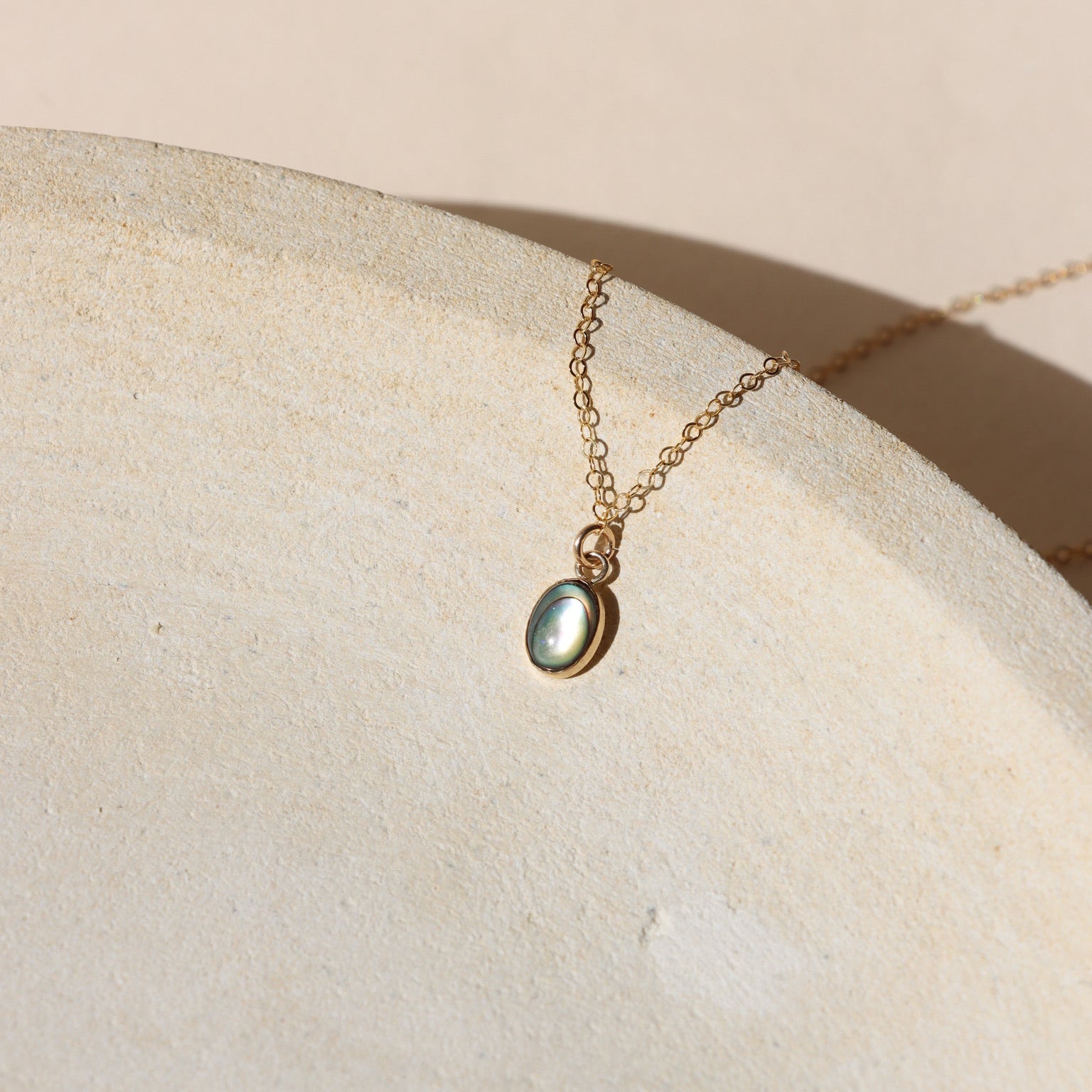 14k gold fill delicate chain necklace with 14k gold fill bezel pendant with an abalone stone on a light dish