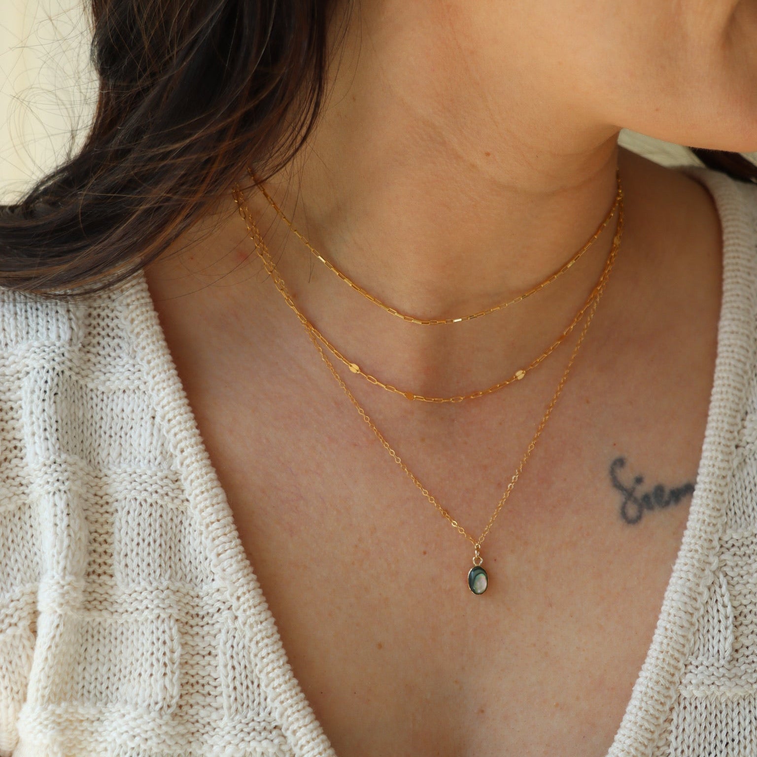 model wearing 14k gold fill chain necklaces with 14k gold fill delicate chain necklace with 14k gold fill bezel pendant with an abalone stone on a light dish