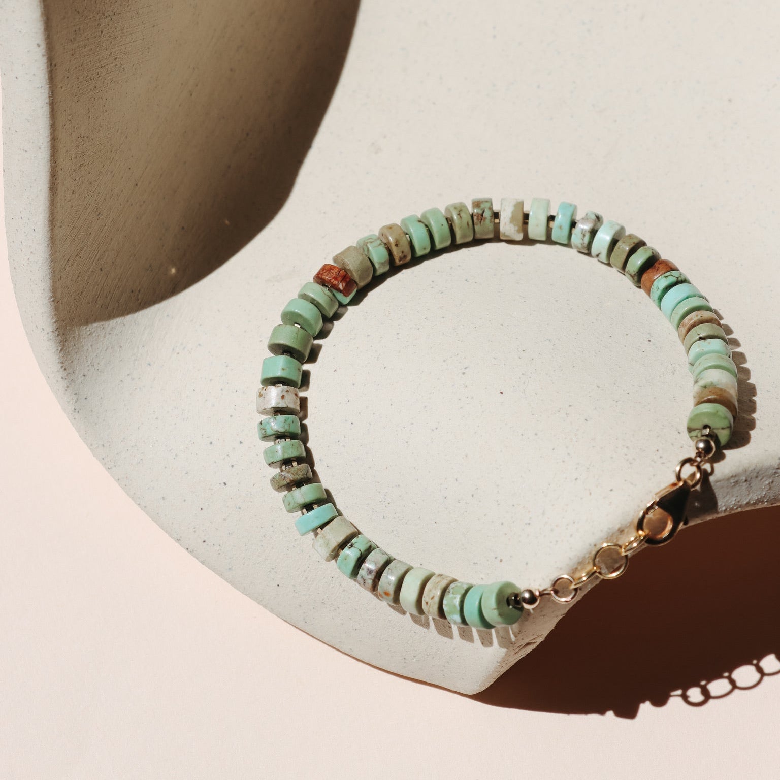 Beaded Turquoise Roundels hand strung into a bracelet draped on a beige ceramic dish in the sunlight