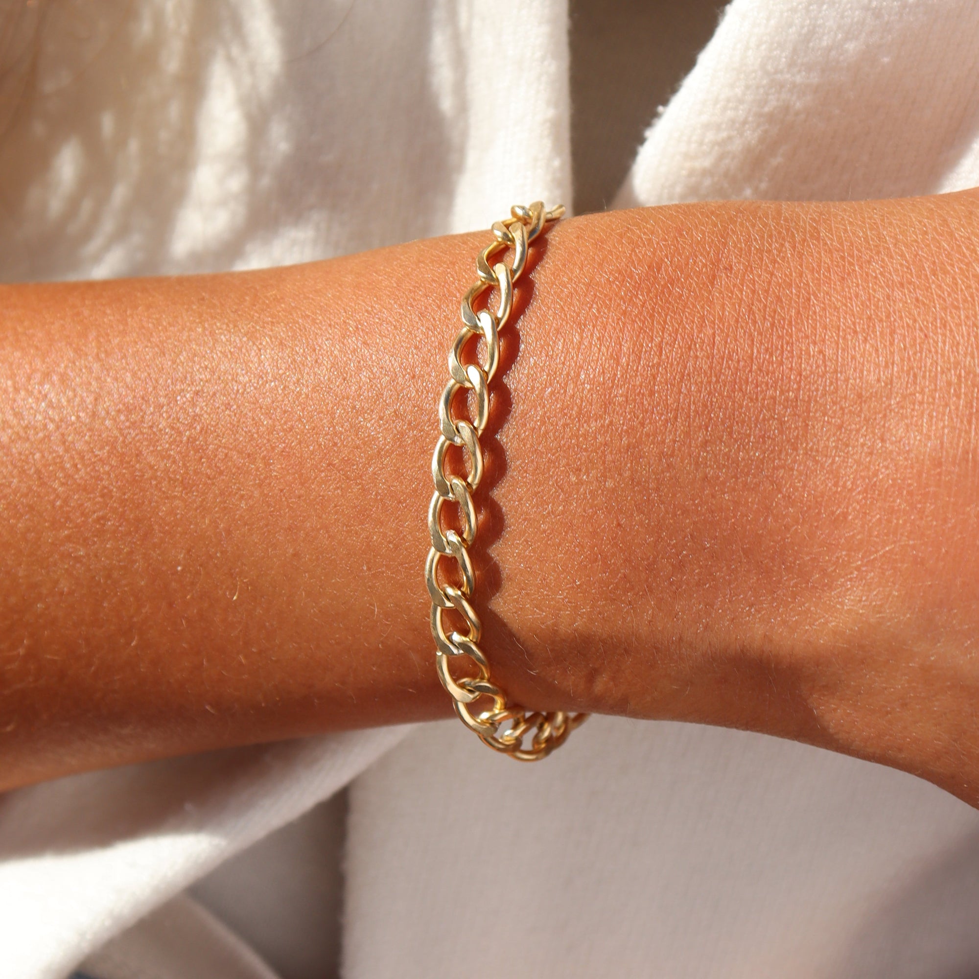 Model wearing a 14k gold fill chunky curb chain bracelet with polished flat links, styled on the wrist in warm natural sunlight.