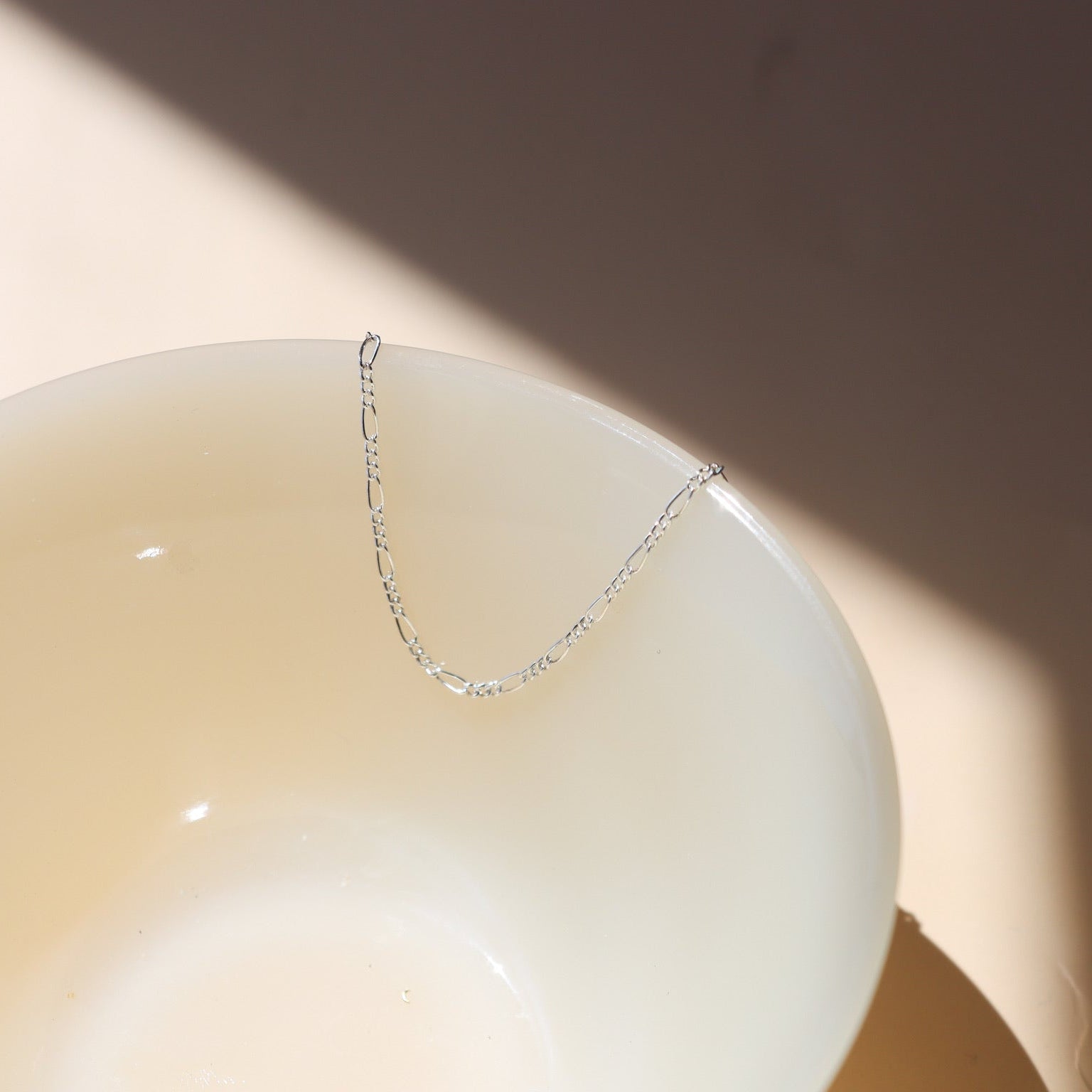sterling silver delicate figaro chain anklet on a light dish