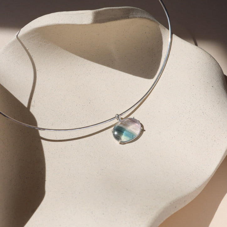 sterling silver wire collarbone necklace with handset fluorite stone in a bezel on a light dish