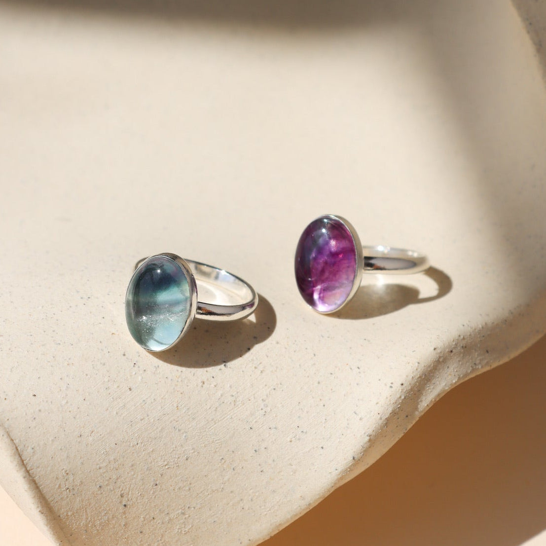 Sterling silver fluorite rings on tan dish in the sunlight.