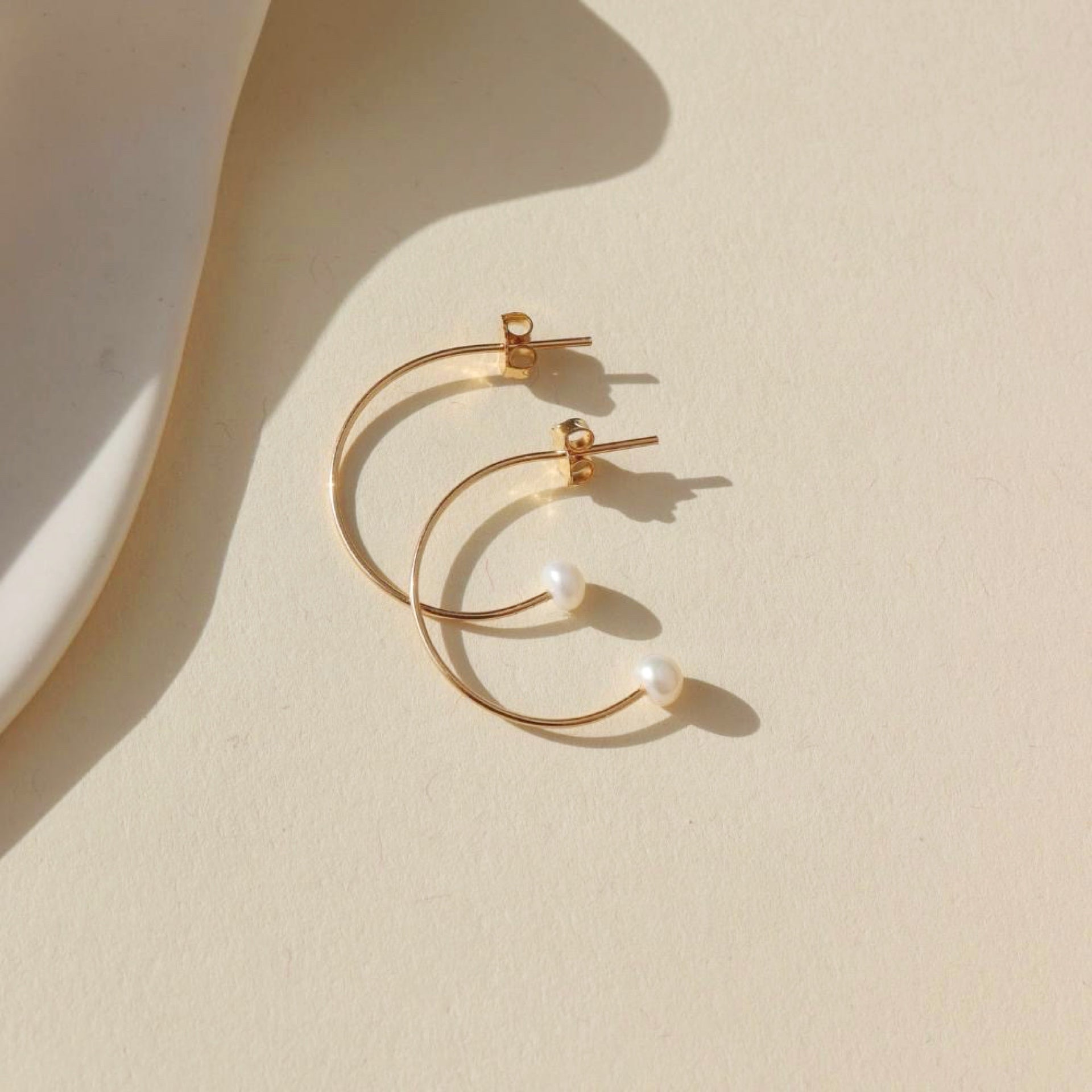 14k gold fill wire hoop earrings with pearls on the ends on a light background