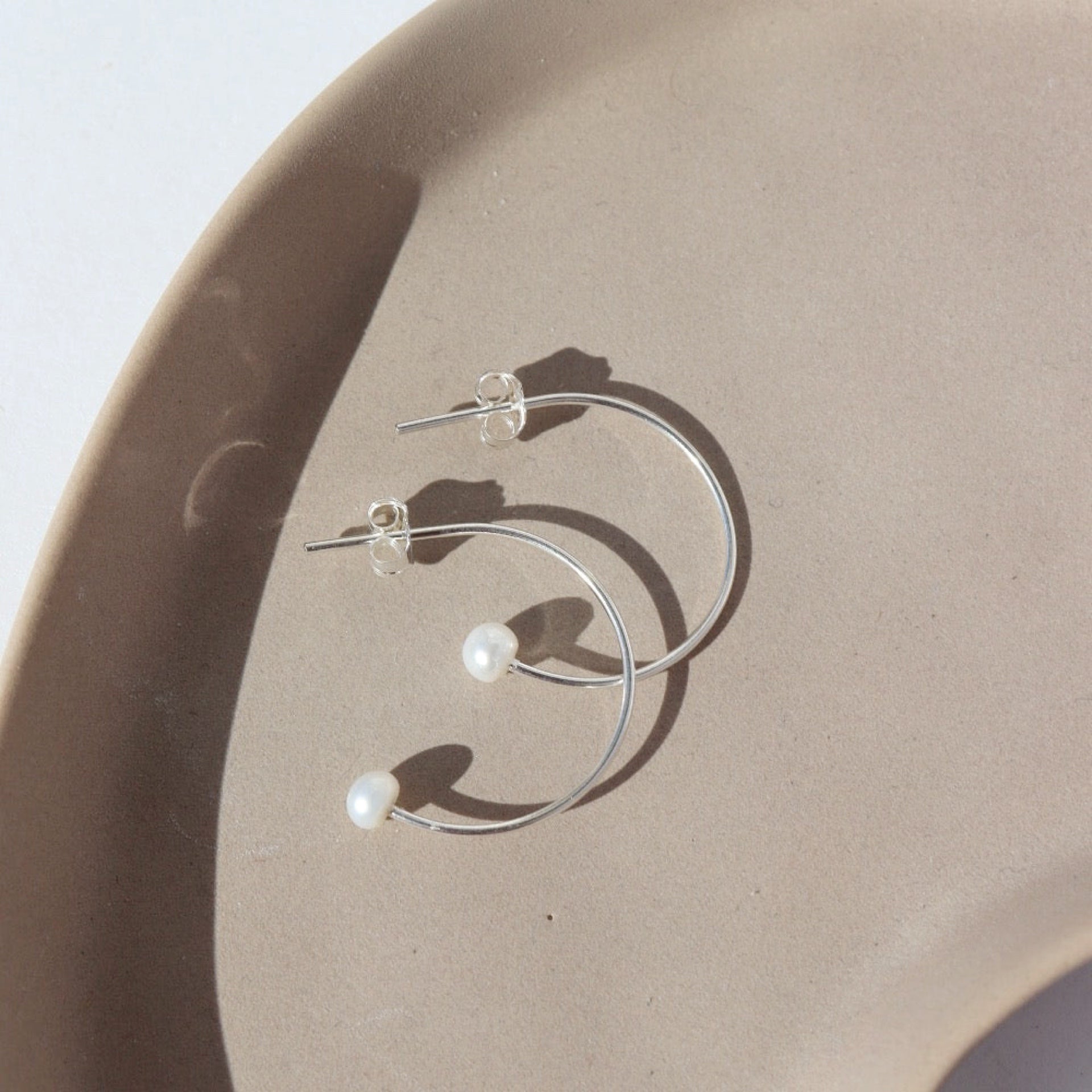 sterling silver wire hoop earrings with pearls on the ends on a light dish
